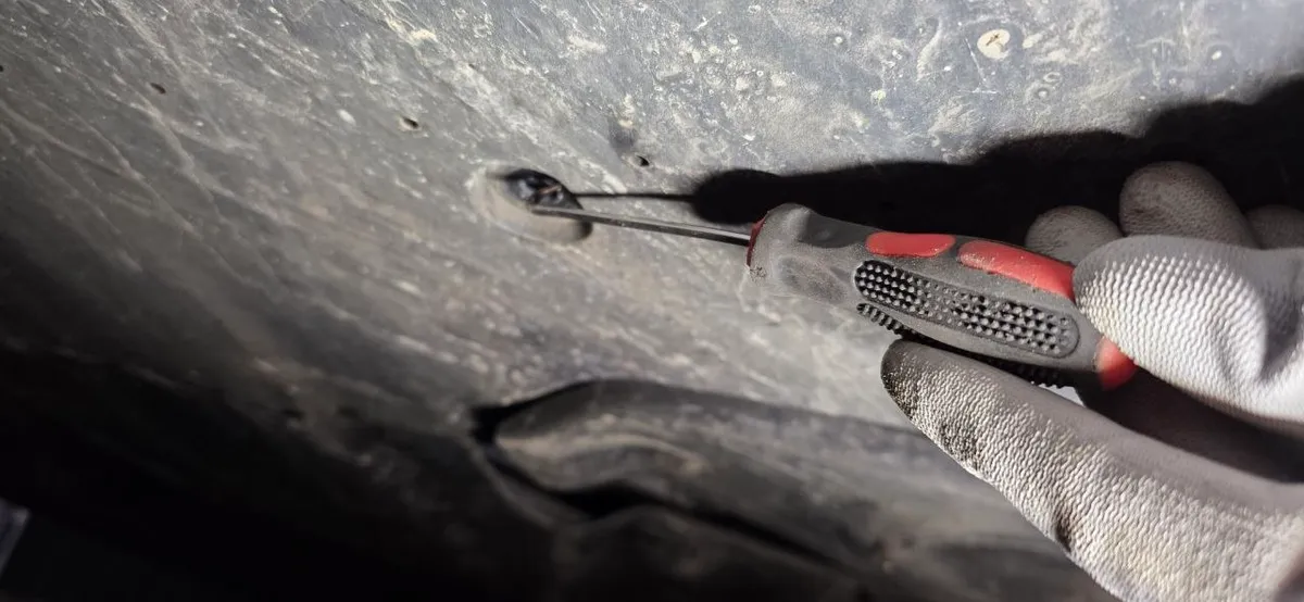 Close-up of an underbody expansion clip being released with a screwdriver