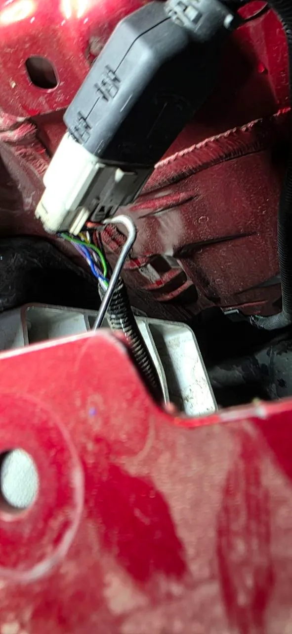 Close-up of the harness connector lock tab being released with a pick