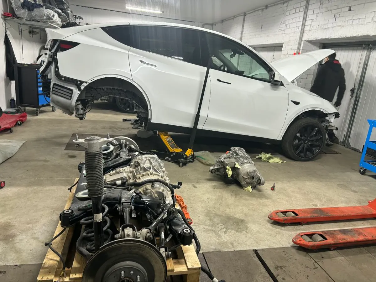 Tesla Model Y with front and rear drive units removed, placed on workshop floor during drivetrain service